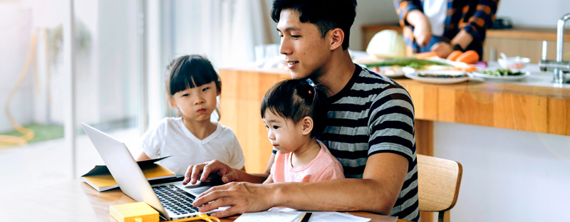 Father using computer to make mortgage payment with daughters watching