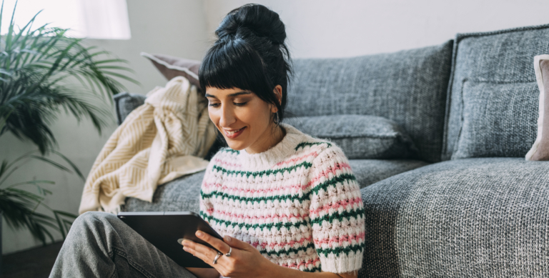 Young woman sitting on the floor, watching a podcast on her tablet.