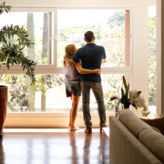 A couple standing in front of a large window in a living room