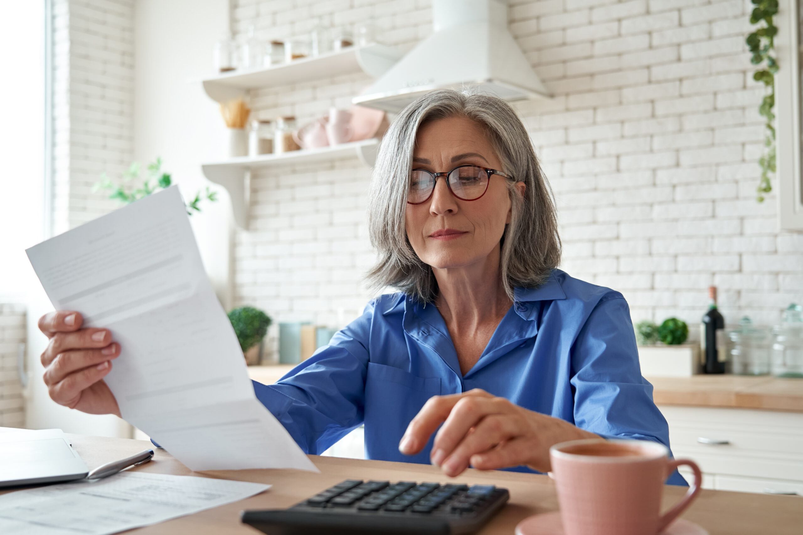 senior woman reviews a paper bill with a calculator at the kitchen table