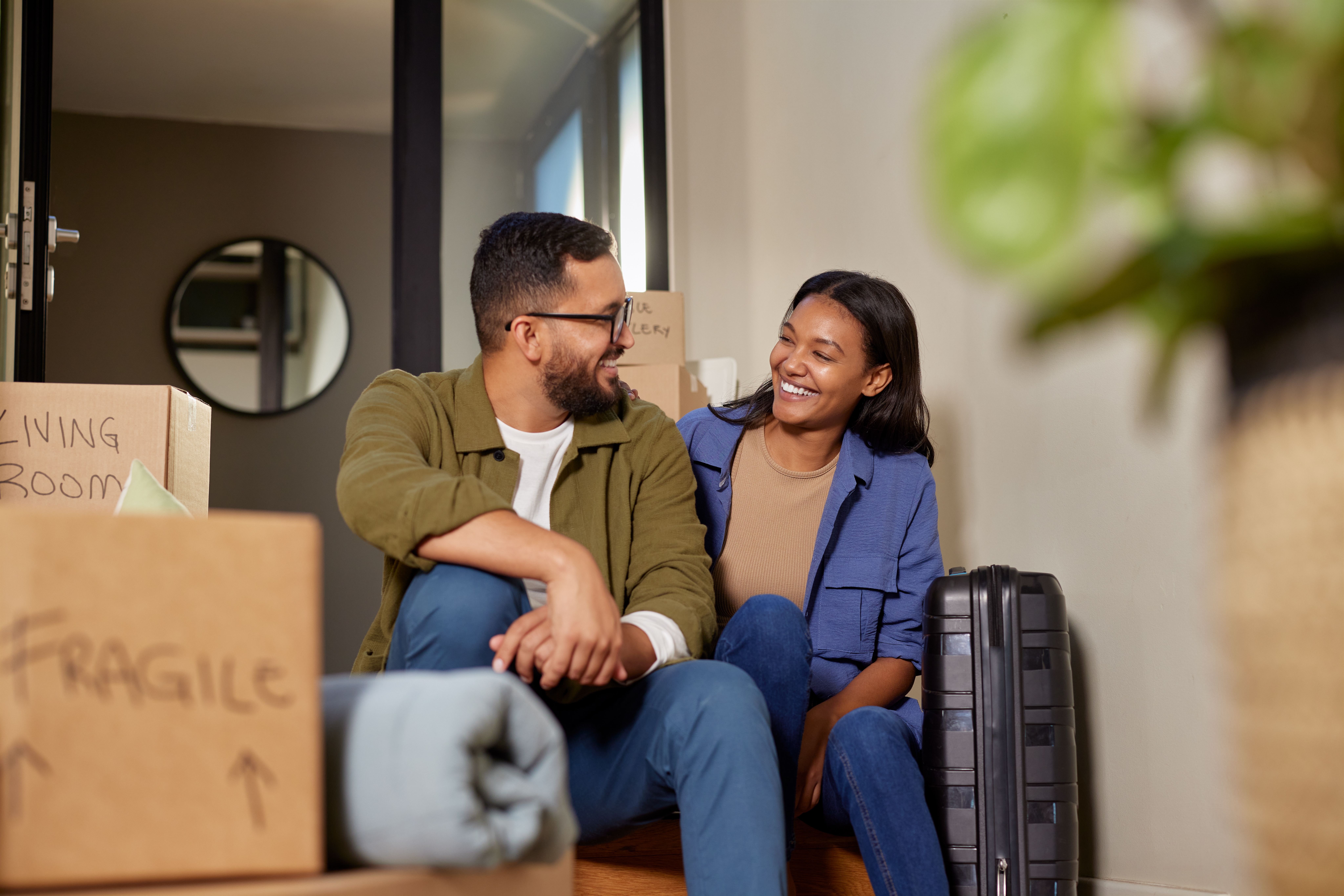 Smiling and happy man and woman sit in their new home surrounded by moving boxes.