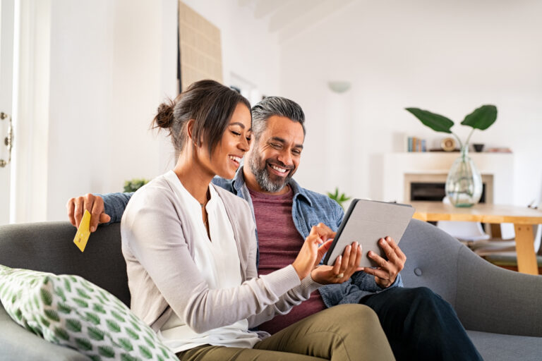 happy couple sit on the couch and pay a credit card bill using funds from their home equity loan