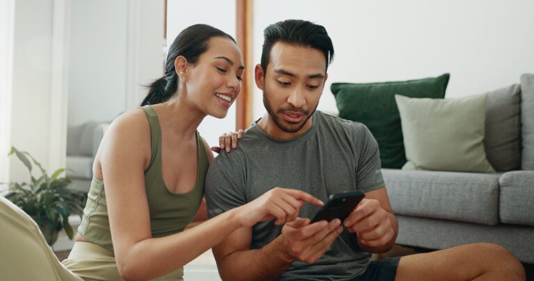 A man in a gray shirt checks his credit score on his phone as his partner points to the screen. 