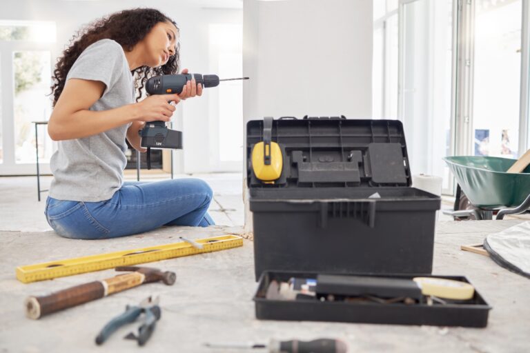 A woman with curly hair uses a power drill during a home renovation.