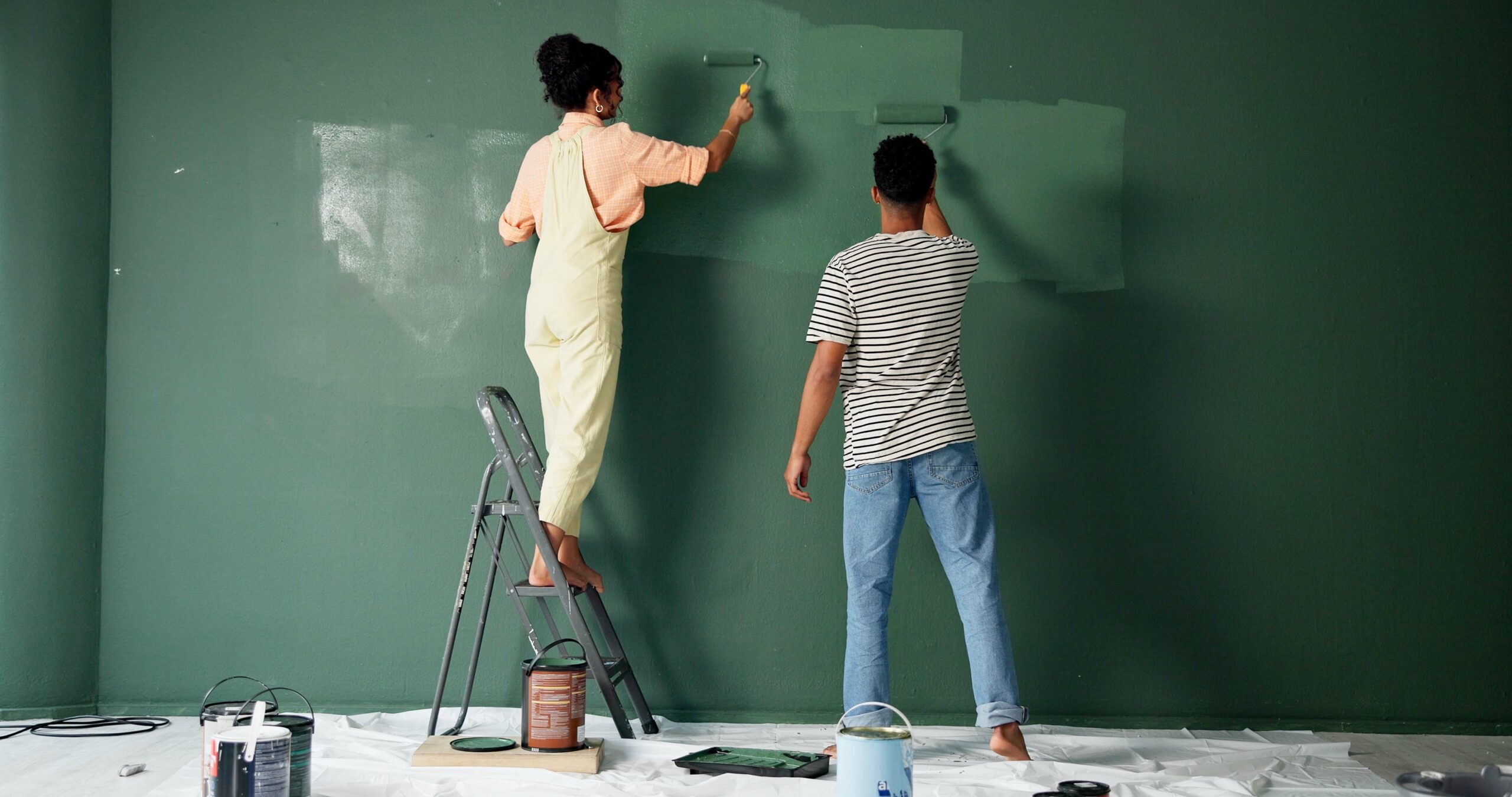 man and woman paint a green wall inside their house